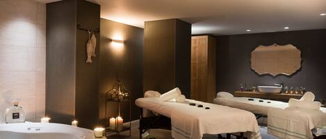 A spa room with two massage tables, a large bathtub, and candles.