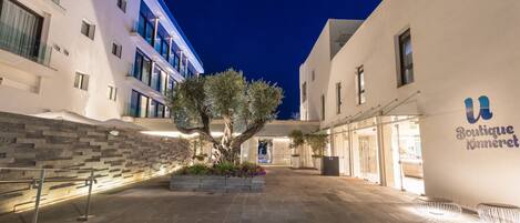 A courtyard with a tree, stone wall, and a building with a sign reading "Boutique Kinneret".