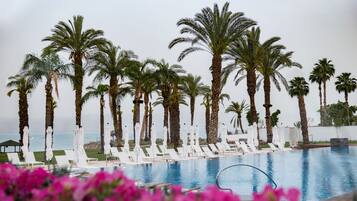 A poolside area with palm trees, lounge chairs, and umbrellas.