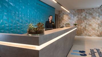 A reception desk with a geometric blue wall, a receptionist, and a patterned wall in the background.