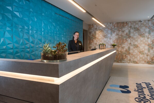 A reception desk with a geometric blue wall, a receptionist, and a patterned wall in the background.