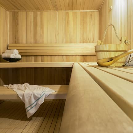 A wooden sauna with benches, a bench with a towel, and a wooden bucket.