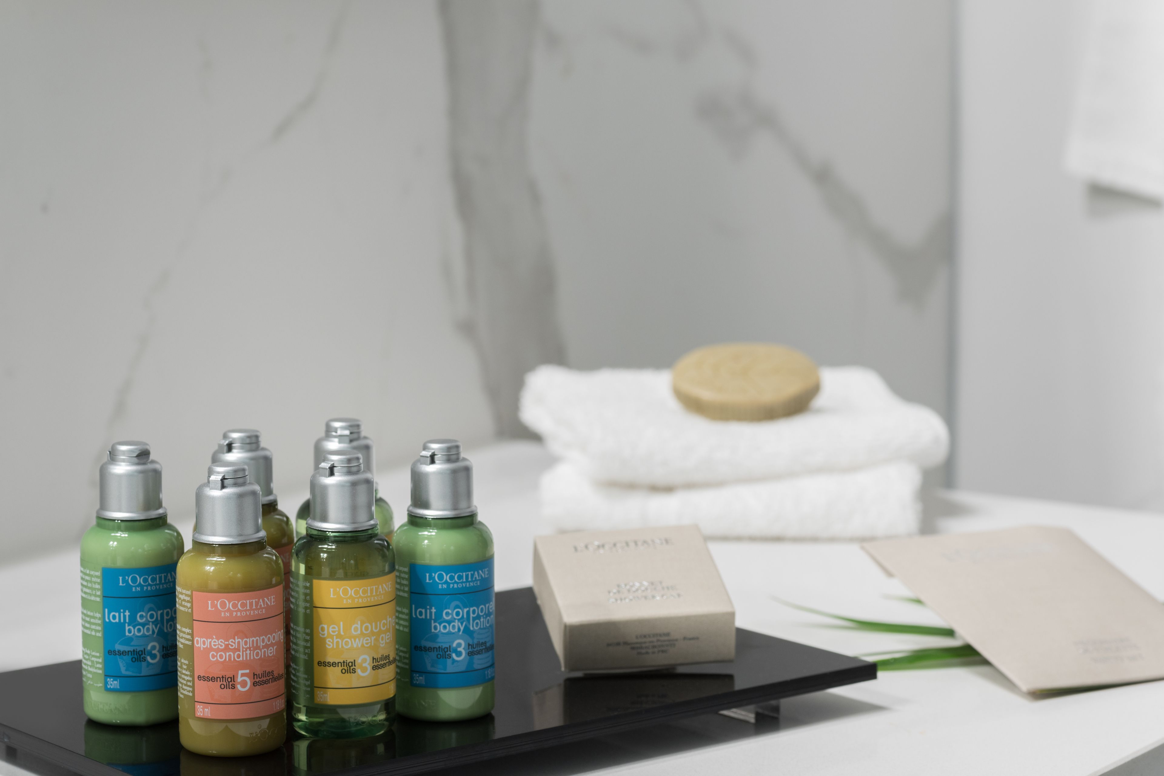 Una encimera de baño con varios productos de cuidado corporal de L'OCCITANE, una barra de jabón y una toalla blanca.