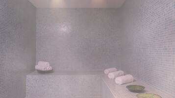 Une salle de bain avec un sol et des murs carrelés, un banc et deux lavabos.