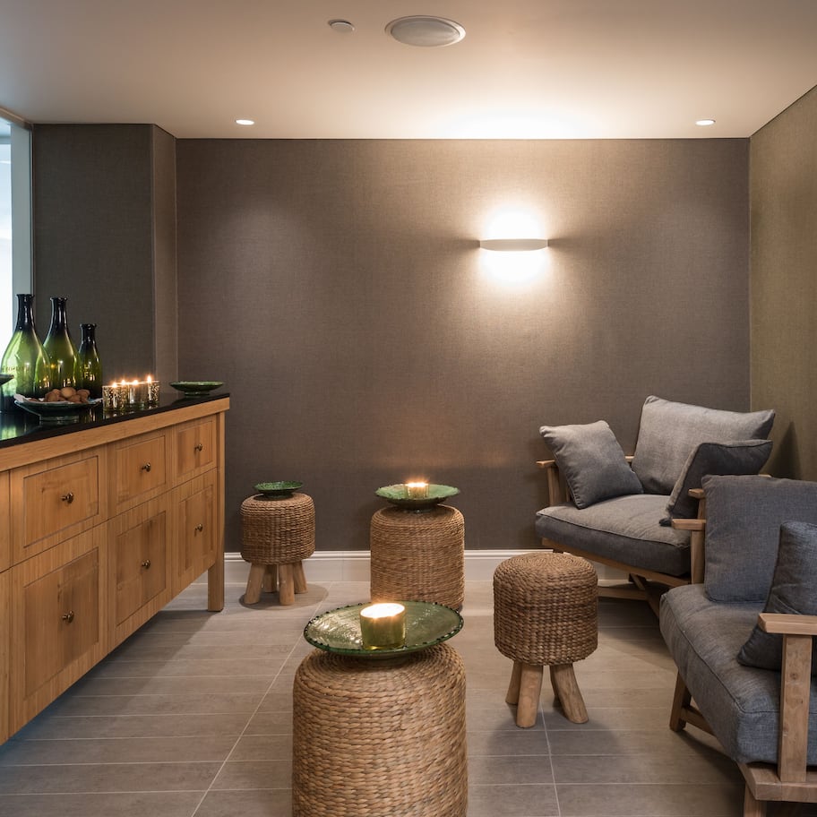A modern living room with a wooden cabinet, wicker ottomans, a grey sofa, and a wall-mounted light fixture.
