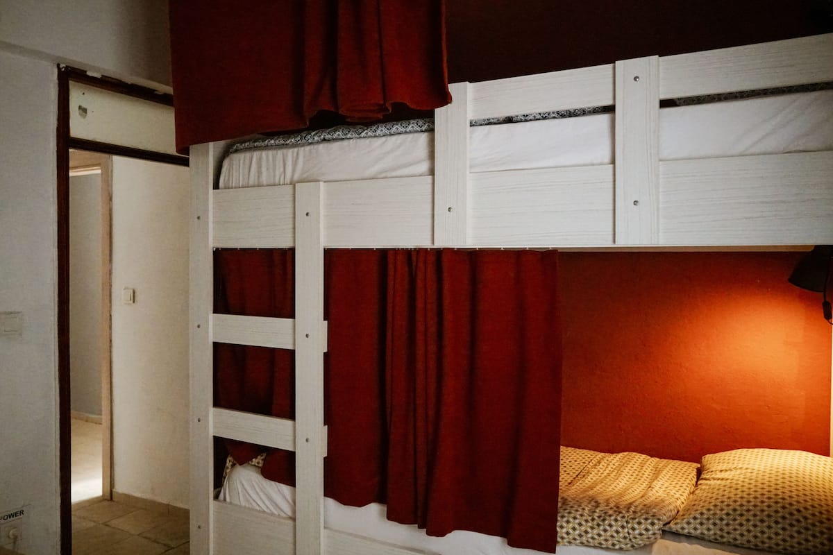 Uma cama beliche com cortinas vermelhas e almofadas estampadas.