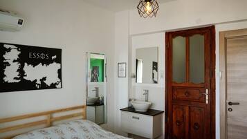 A bedroom with a bed, a bedside table, a mirror, a wooden door, and a wall-mounted air conditioner.