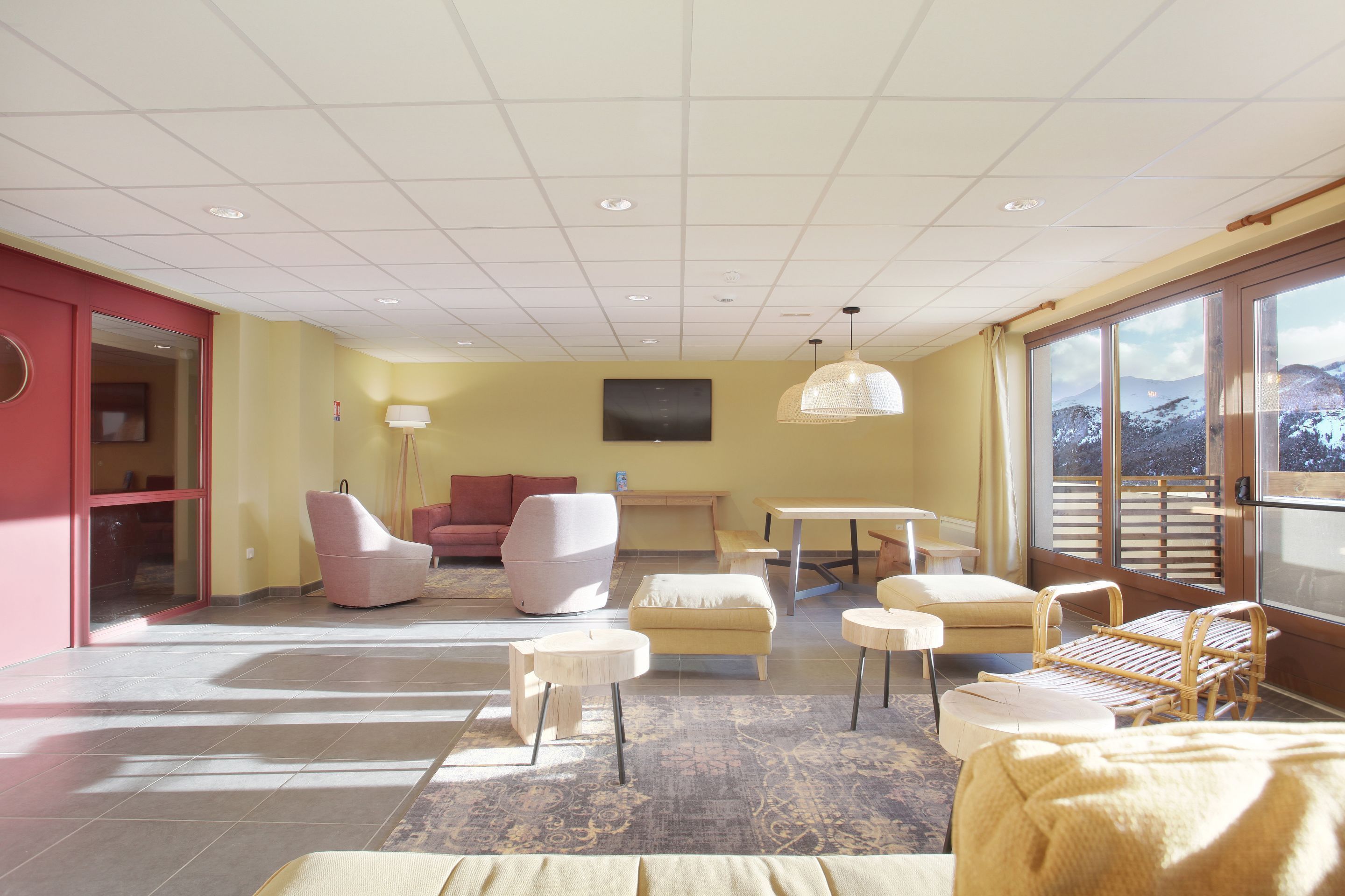 Un salon moderne avec un canapé, des fauteuils, une table basse et une vue sur un paysage enneigé, visible à travers de grandes fenêtres.