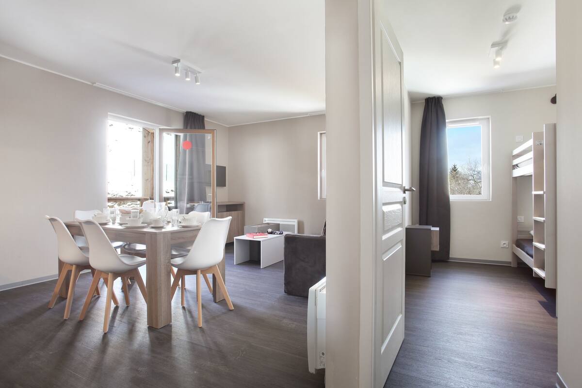 A modern, well-lit room with a dining table, chairs, a sofa, and a bed.