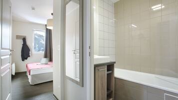 A modern bathroom with a bathtub, a shower area, and a toilet. There is a window with a view of mountains in the background.