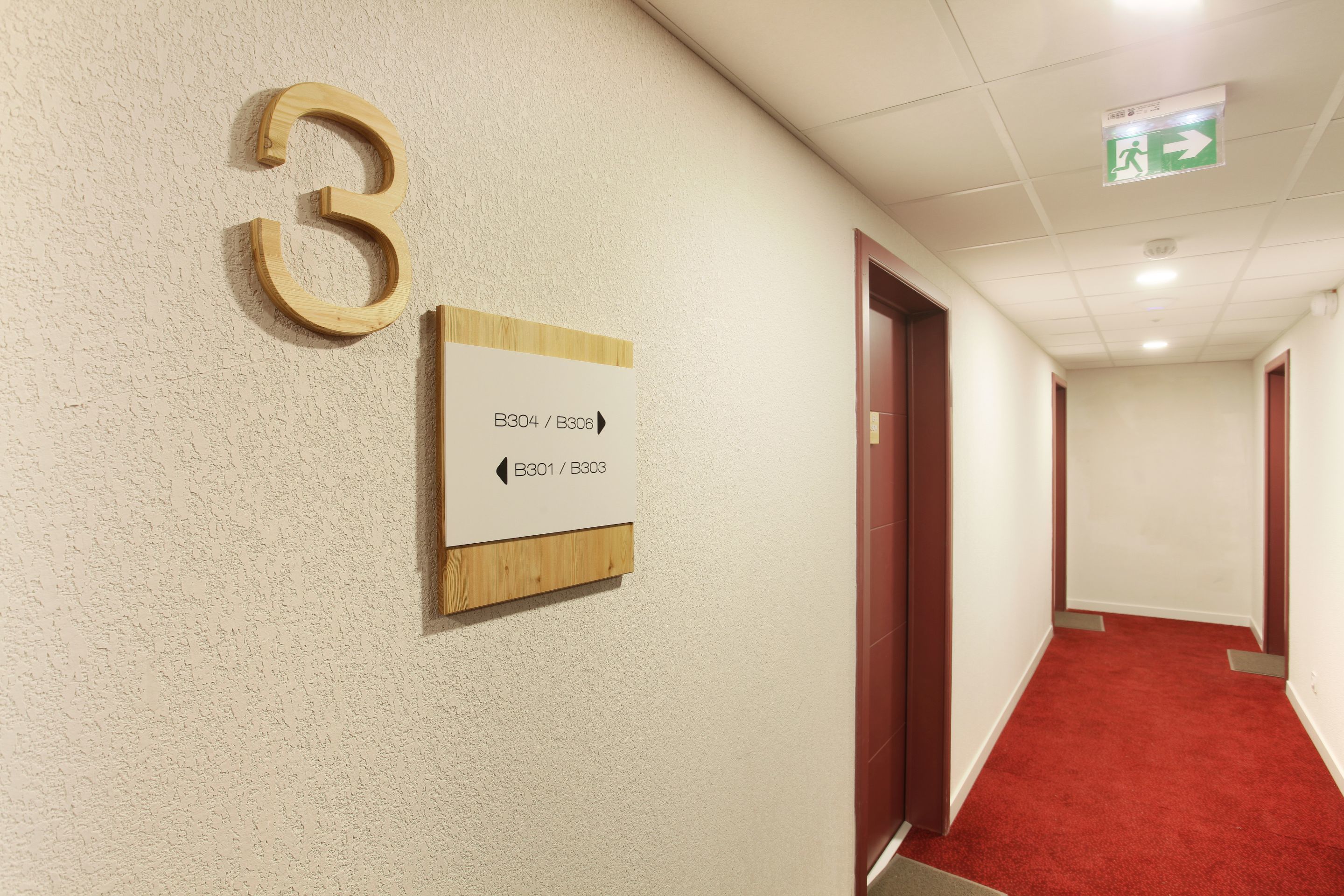 A hallway with a number '3' sign, directional arrows, and emergency exit sign.