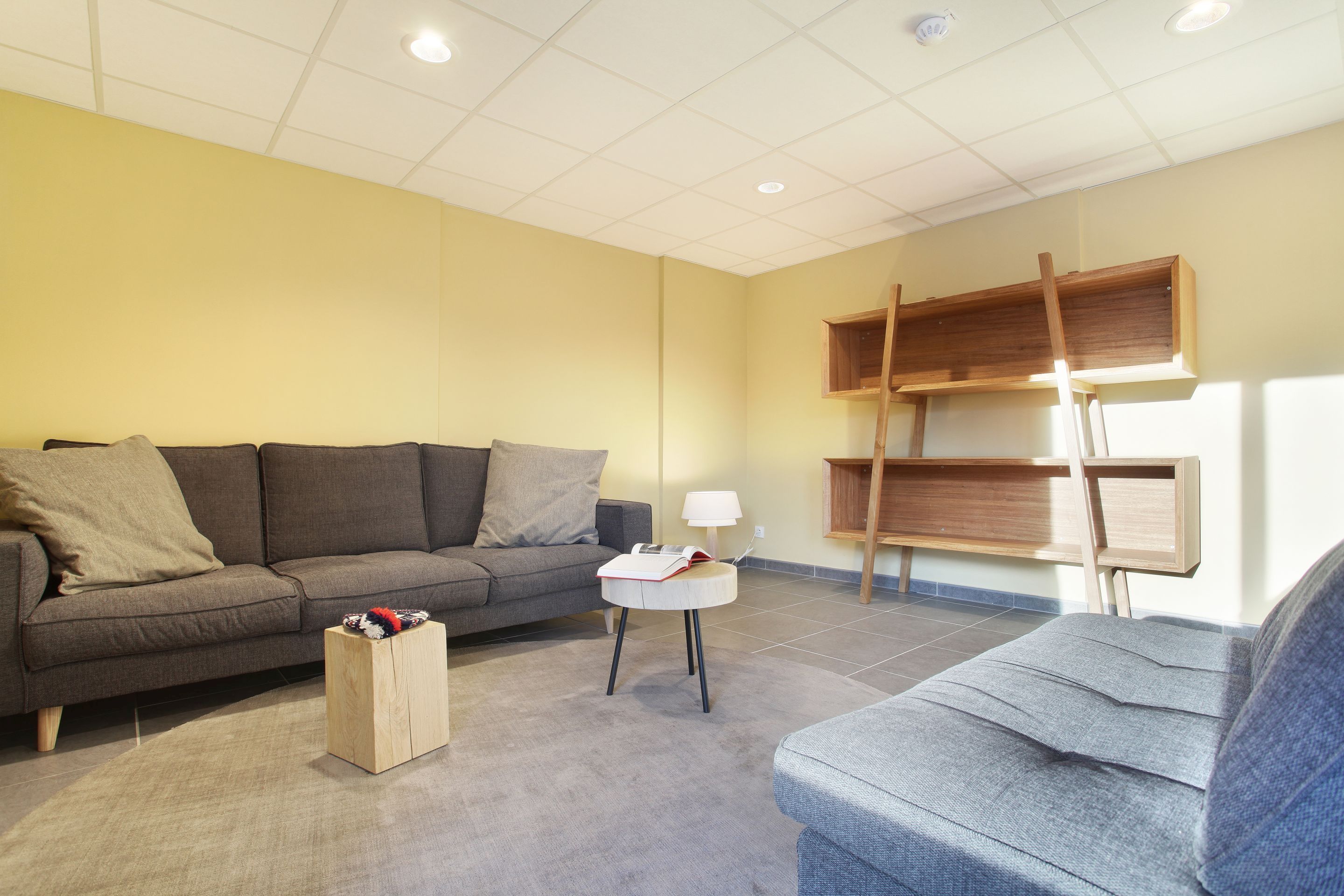 A living room with a grey sofa, a small wooden side table, and a lamp.