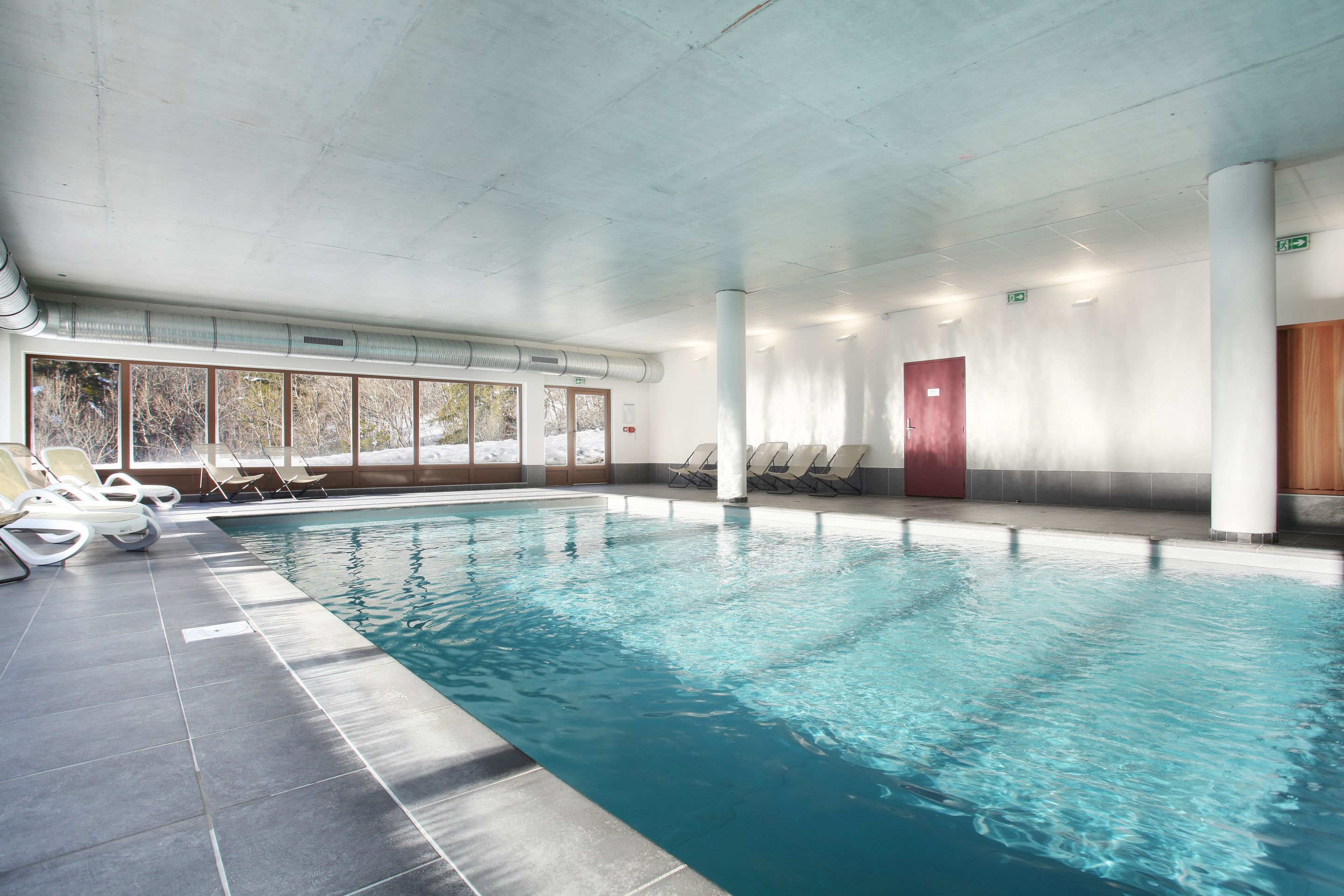 Una piscina interior con agua cristalina, suelo de baldosas y sillones de descanso a lo largo del borde.