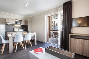 A modern kitchen with a microwave, toaster, and coffee machine. There is a dining area with a table and chairs. A TV is mounted on the wall. - Odalys Residence le Village du Praroustan (Uvernet-Fours)