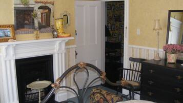 A bedroom with a fireplace, a bed, a dresser, a chair, and a door leading to a hallway.
