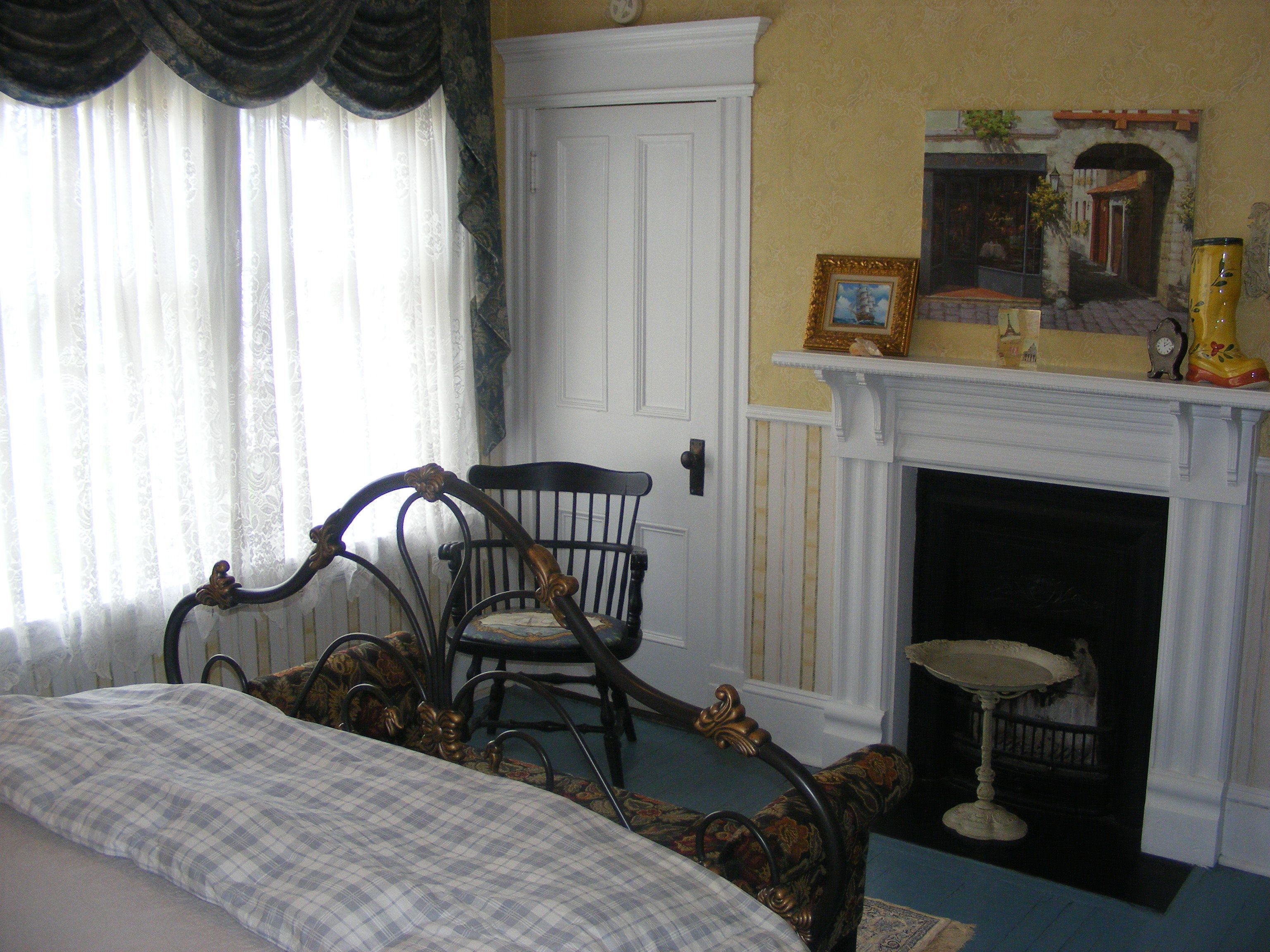 A room with a bed, a chair, a fireplace, and a painting on the wall.