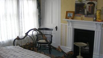 A room with a bed, a chair, a fireplace, and a painting on the wall.