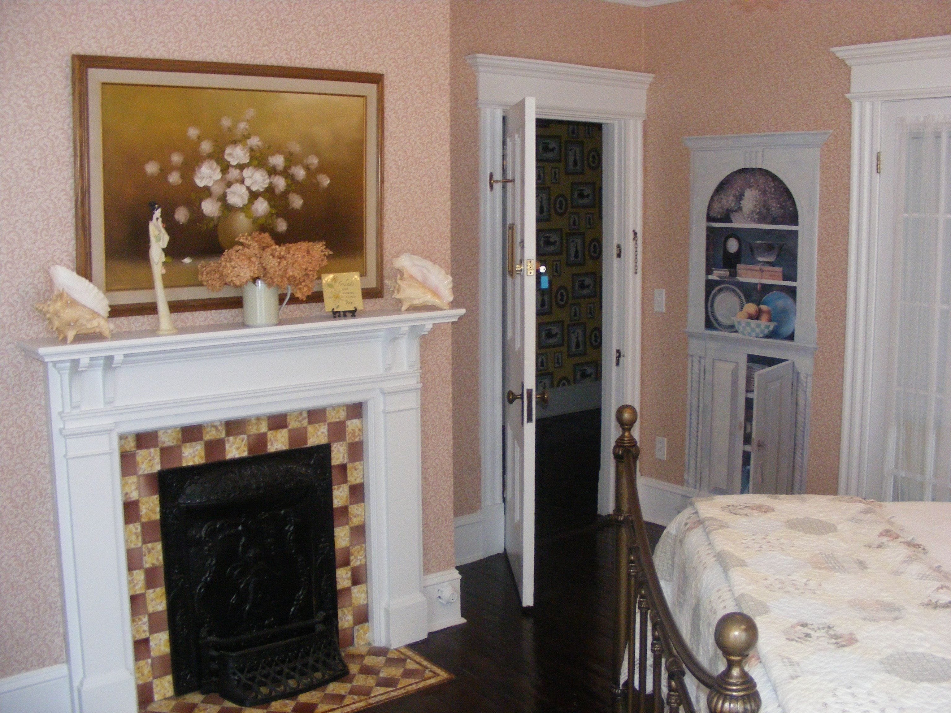 A bedroom with a fireplace, a bed, and a door leading to another room.
