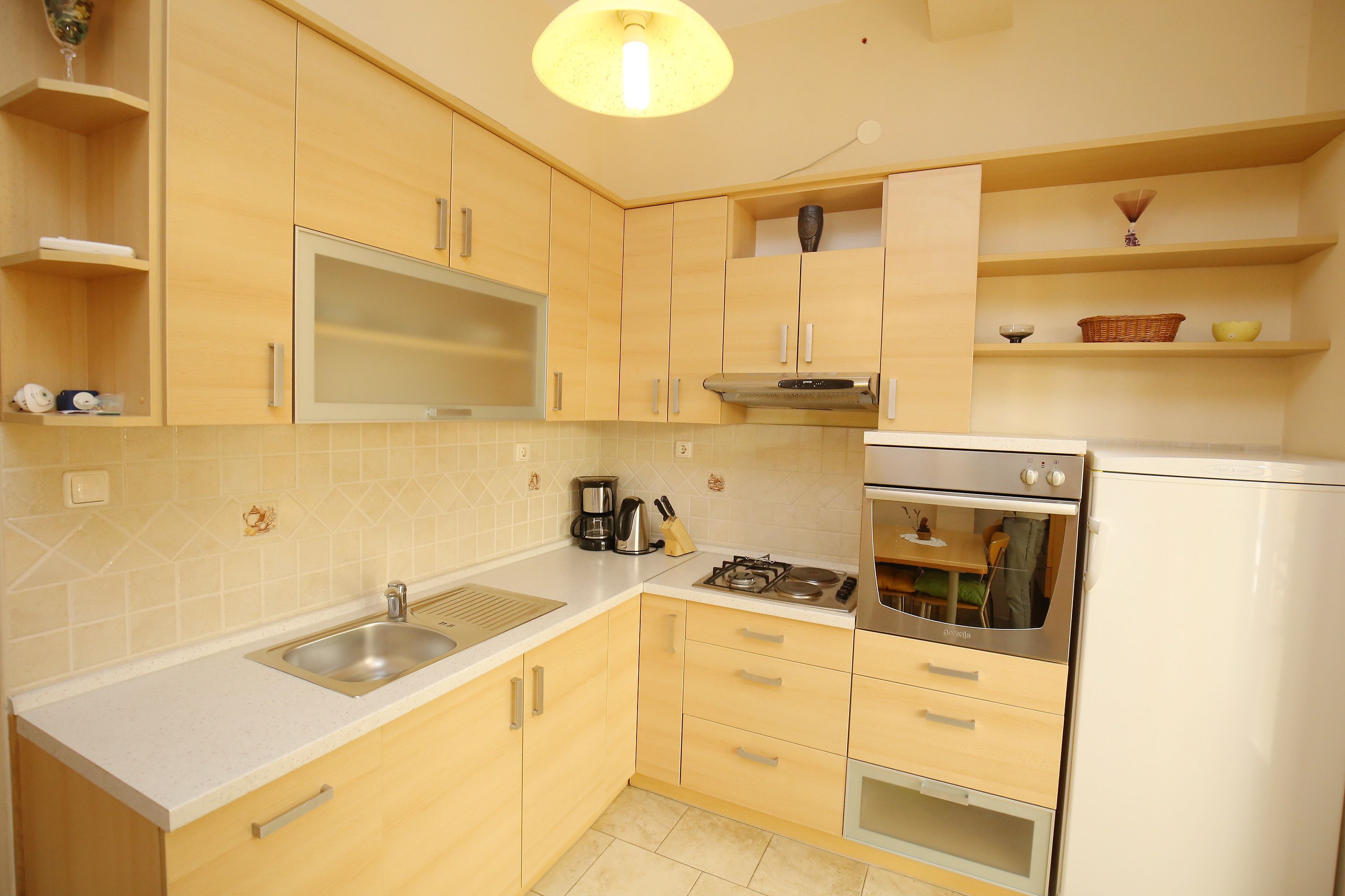 A modern kitchen with light wood cabinets, a stainless steel sink, a built-in oven, and a gas stove.