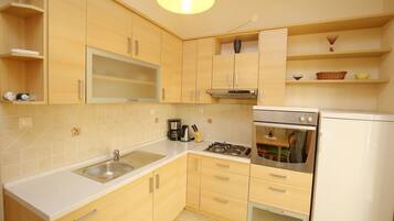 A modern kitchen with light wood cabinets, a stainless steel sink, a built-in oven, and a gas stove.