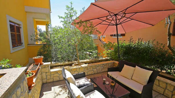 Eine Terrasse im Freien mit Korbmöbeln, einem Glastisch und einem großen roten Sonnenschirm.