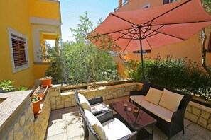 An outdoor patio with wicker furniture, a glass table, and a large red umbrella.