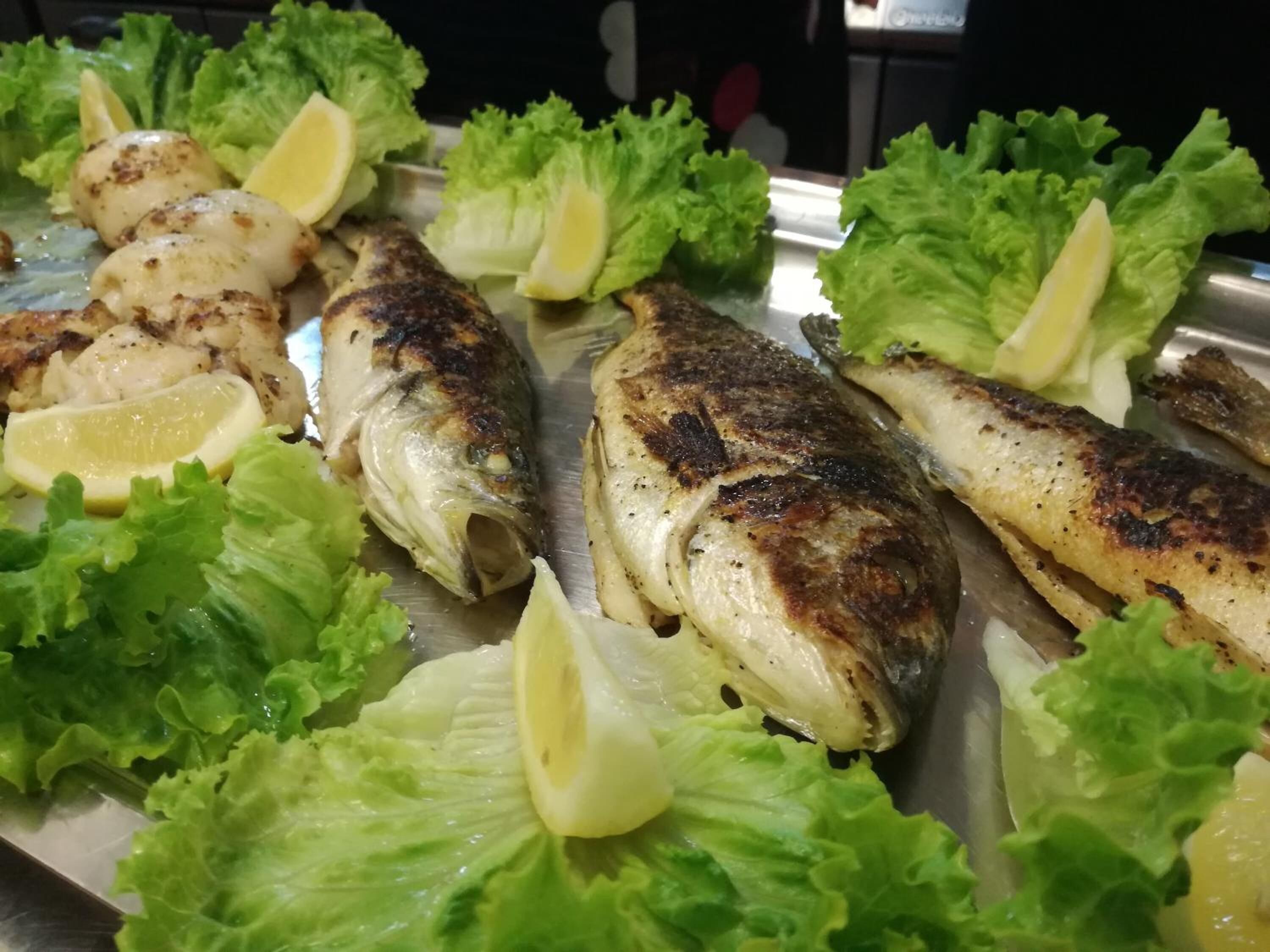 Grilled fish and lemon slices on a tray with lettuce.