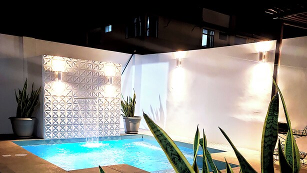 A pool area with a geometric wall design, potted plants, and a sign for Costa Verde HOSTAL. - Hostal Costa Verde (Manta)