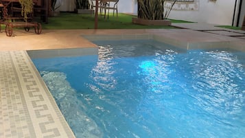 A pool area with a tiled edge, a small table with chairs, and a potted plant.