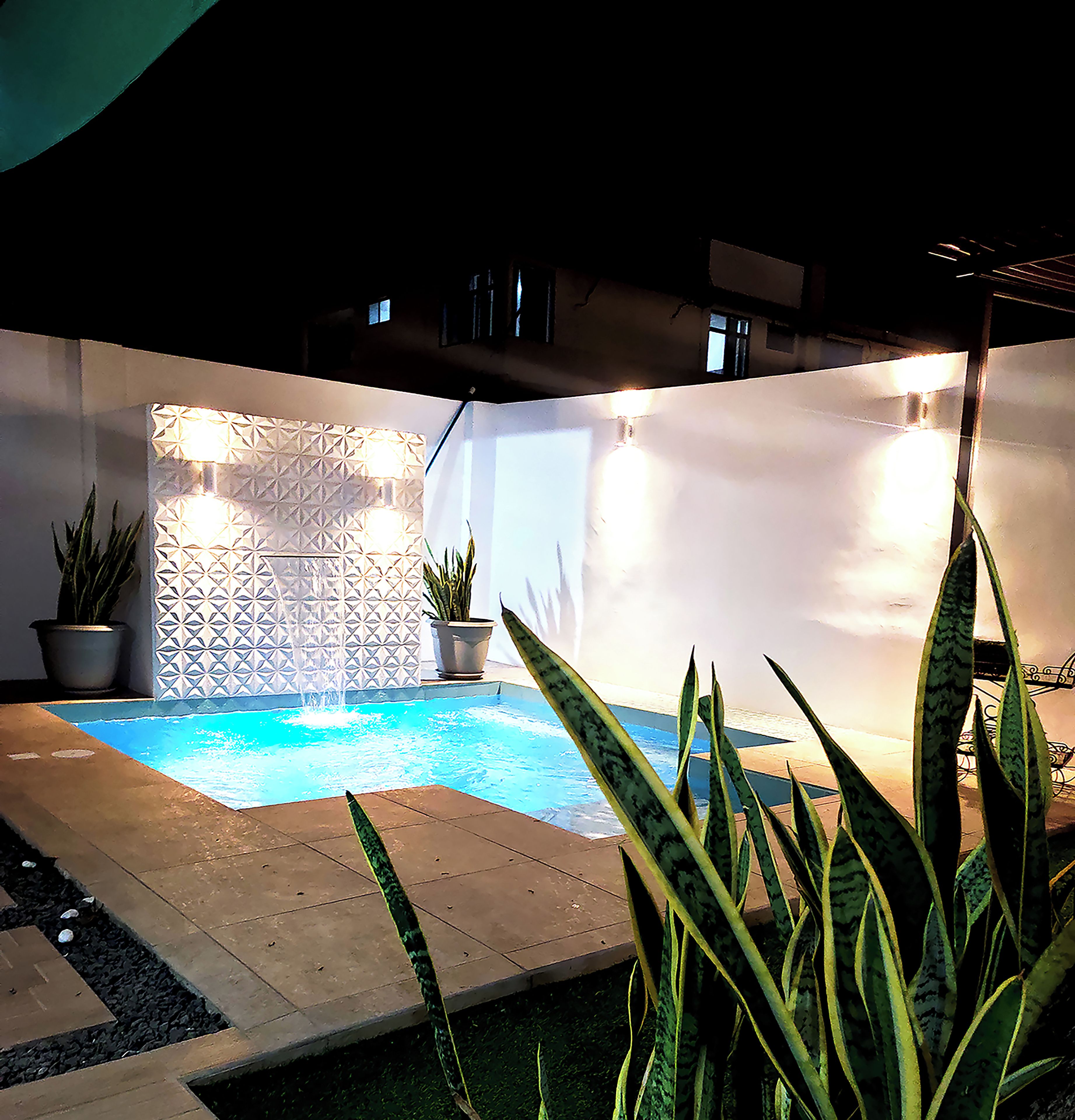 A pool area with a geometric wall design, potted plants, and a sign for Costa Verde HOSTAL.