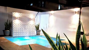 A pool area with a geometric wall design, potted plants, and a sign for Costa Verde HOSTAL.