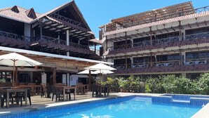 Um hotel com piscina, área de estar externa e um pátio coberto.