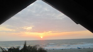 Vista da praia a partir de um espaço coberto, com o oceano e o pôr do sol à mostra.