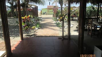 Un área de patio techada con piso de baldosas, un espacio de descanso con mesas y sillas, y vista a la playa al fondo.