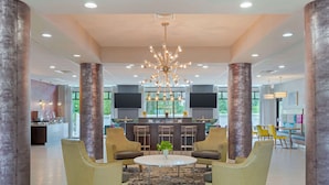 A spacious lobby with a central seating area, a modern chandelier, and a bar with large screens.
