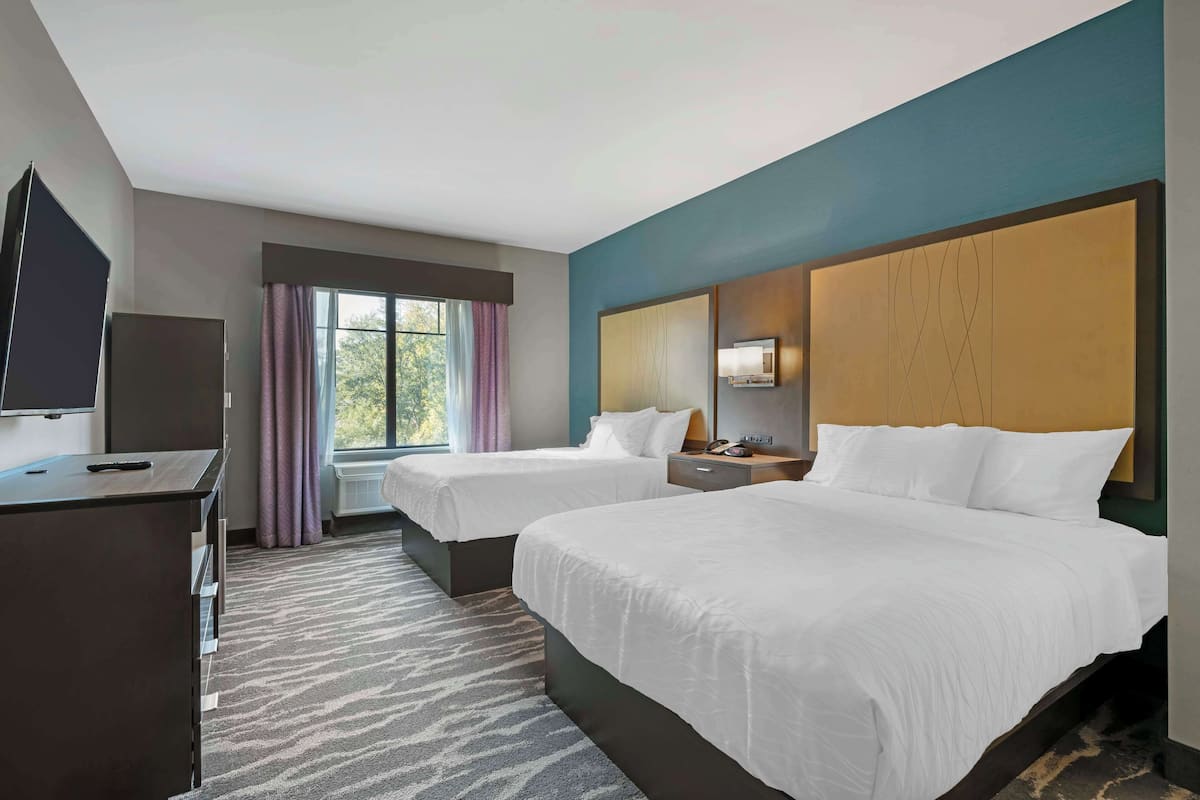 A hotel room with two beds, a desk, a television, and a window with curtains.