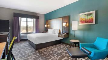 A hotel room with a large bed, a desk, a chair, a small table, and a TV.