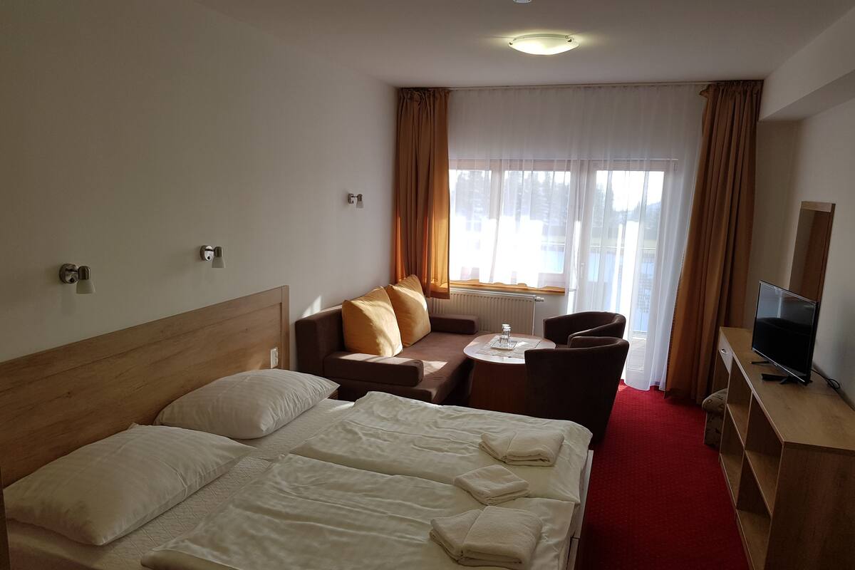 A hotel room with a bed, a sofa, a small table, a TV, and a window with curtains.