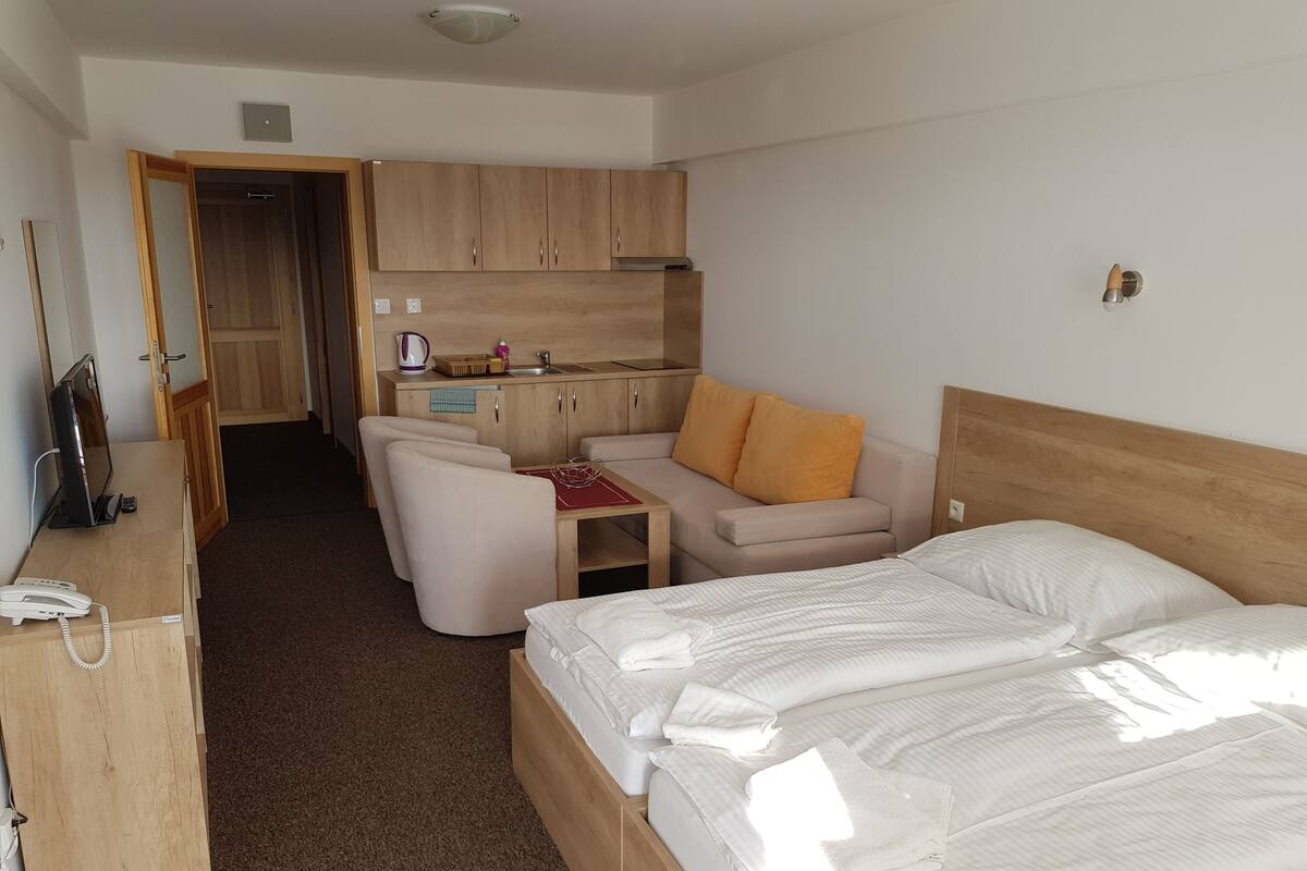 A compact hotel room with a bed, a small kitchenette, a seating area with a table and chairs, and a desk with a phone.