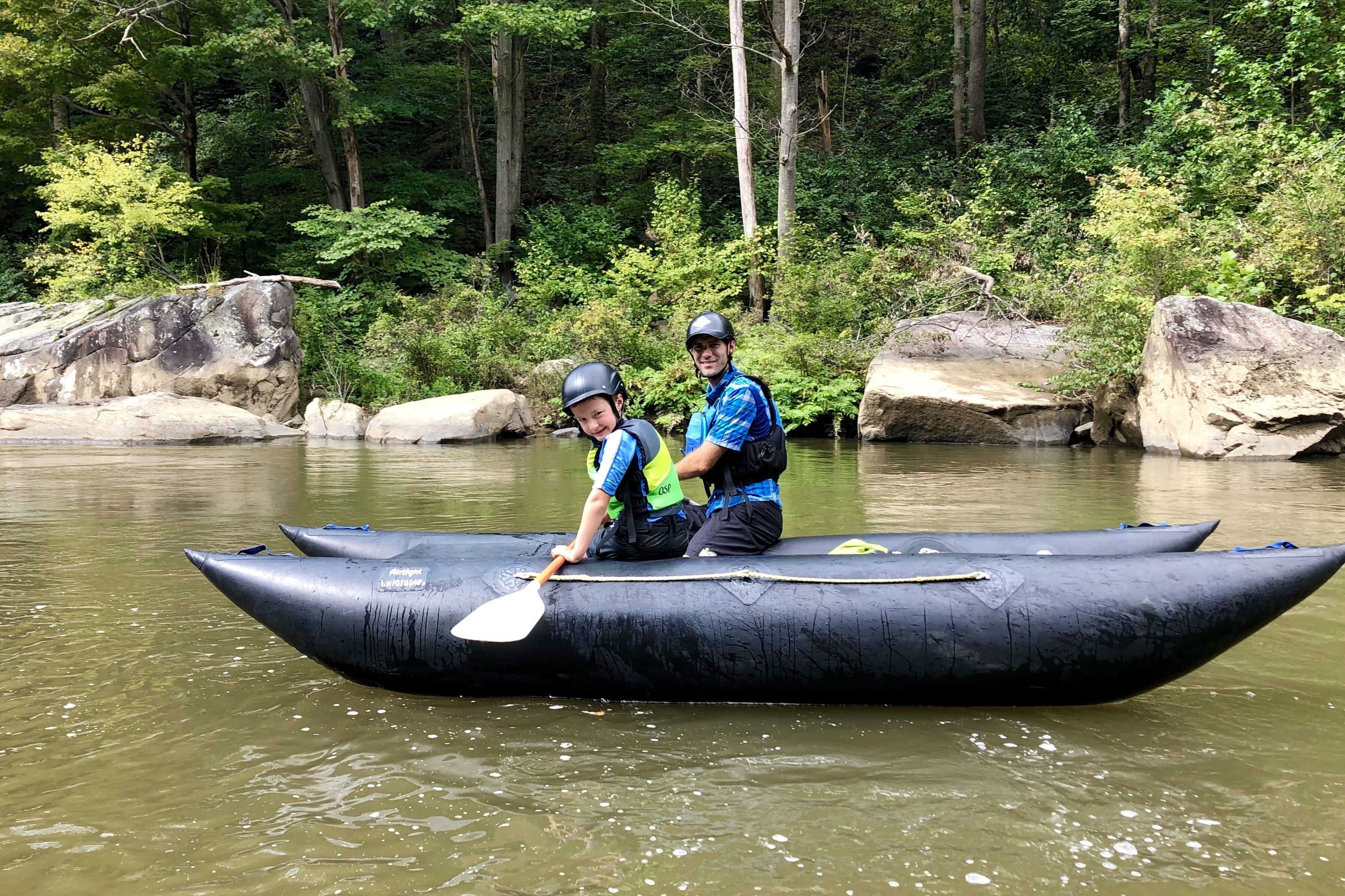 Dos personas en una balsa inflable negra sobre un río rodeado de rocas y vegetación.
