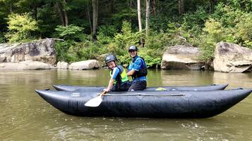 Dos personas en una balsa inflable negra sobre un río rodeado de rocas y vegetación.