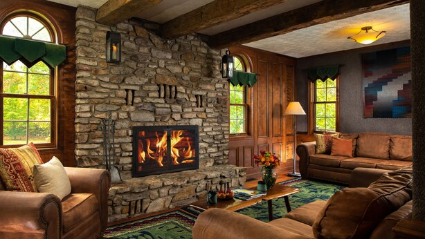 A cozy living room with a stone fireplace, leather sofas, and a large window with a view of trees. - Paddler's Lane Retreat (Confluence)