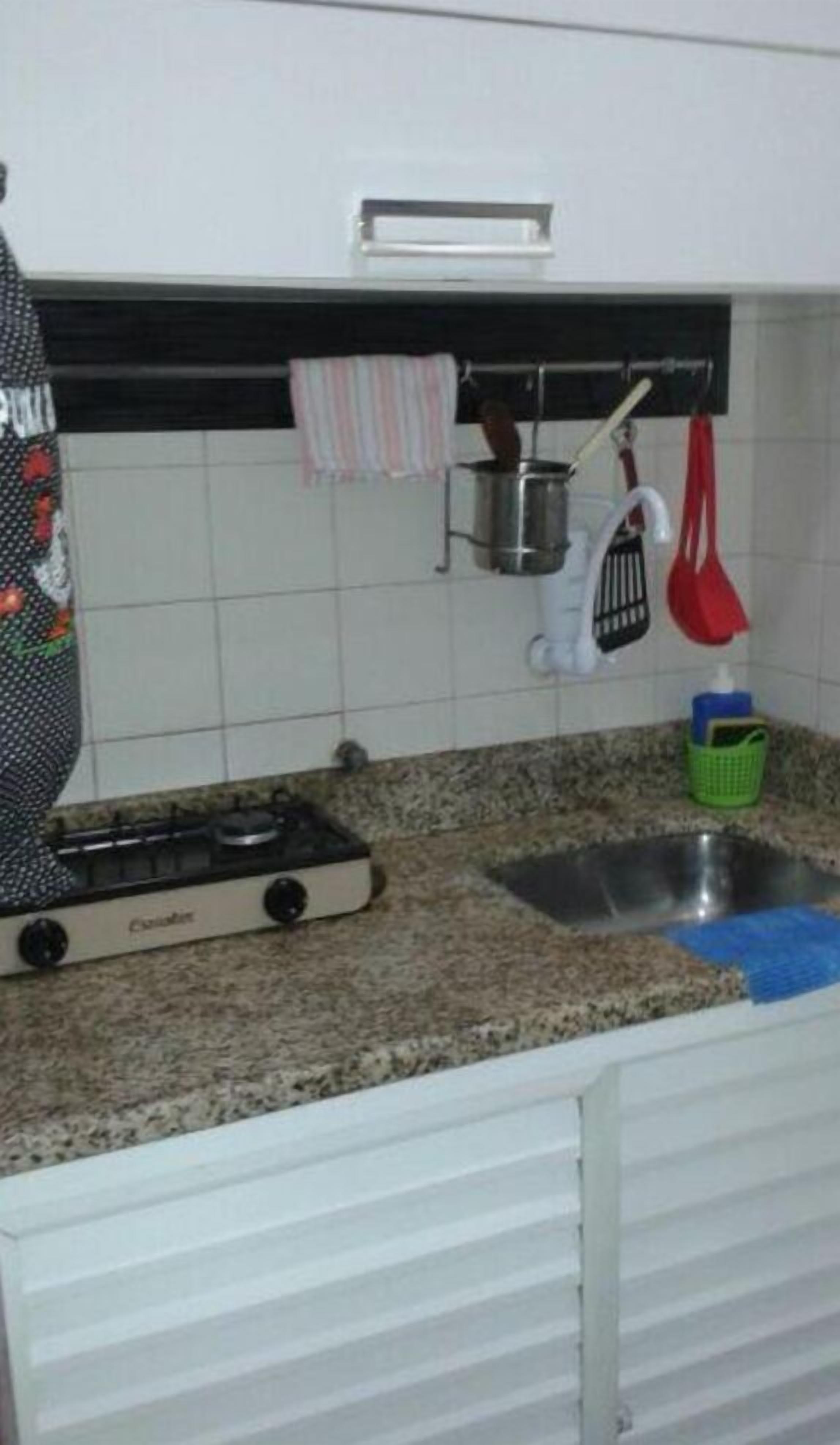 A kitchen with a gas stove, a sink, and hanging kitchen utensils.