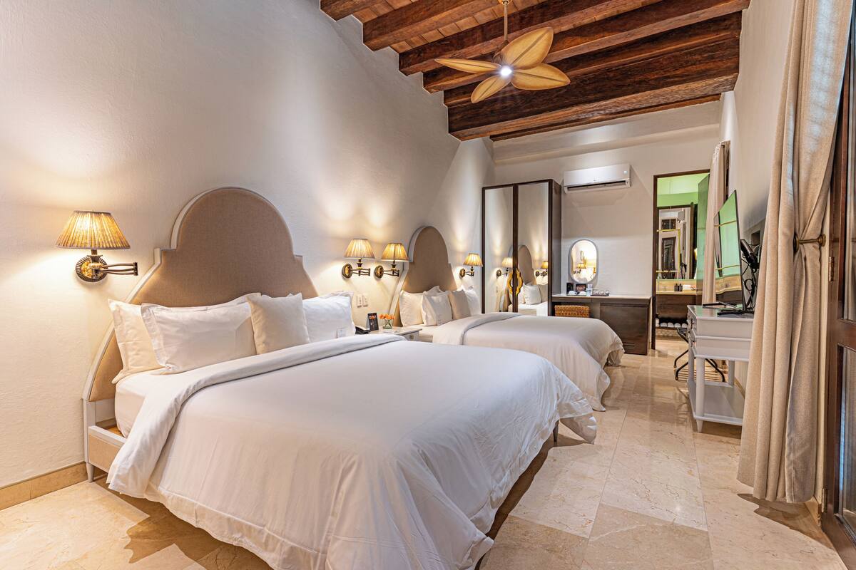 Habitación de hotel con dos camas, un escritorio, un espejo y un ventilador de techo.