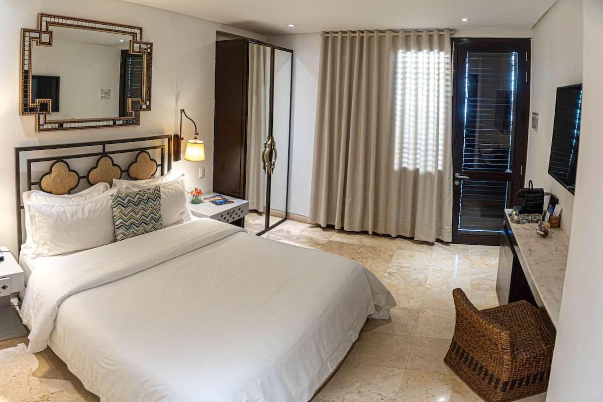 Habitación de hotel con una cama grande, lámparas de noche, un espejo, televisión y una puerta con cortinas.