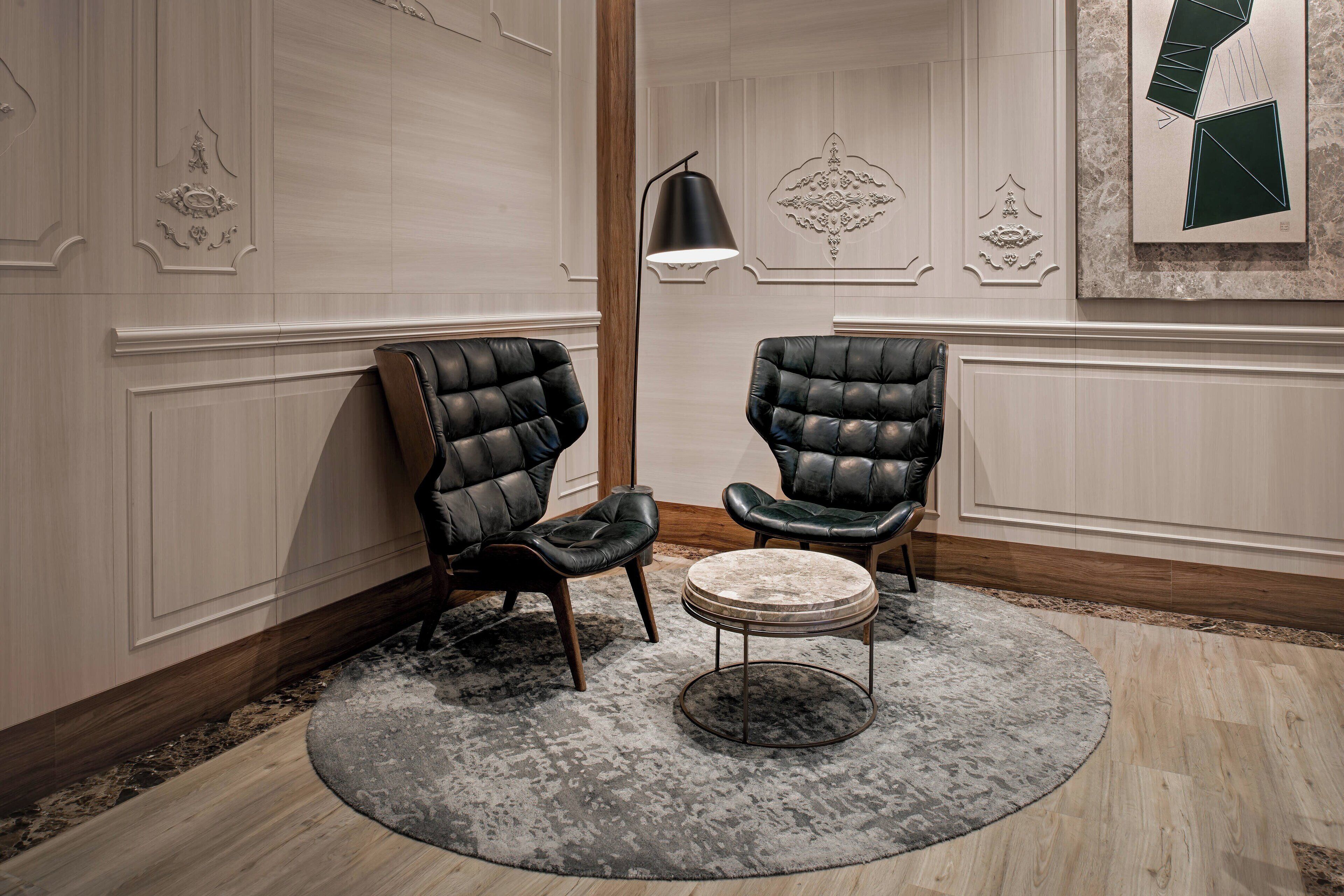 A room with two leather armchairs, a round table, a modern floor lamp, and decorative wall panels.