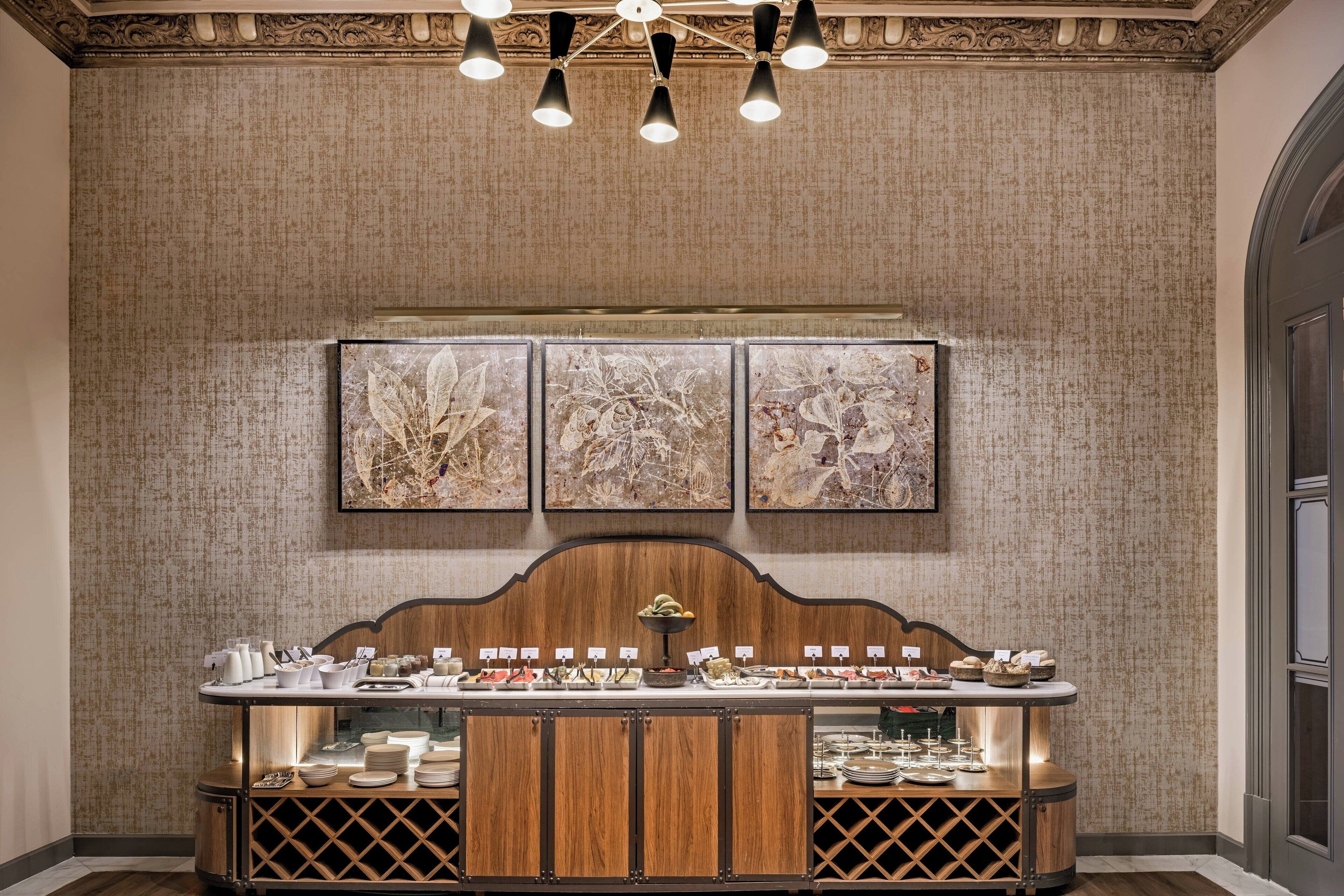 Una barra buffet de madera, con diversos alimentos y tres obras de arte enmarcadas en la pared.