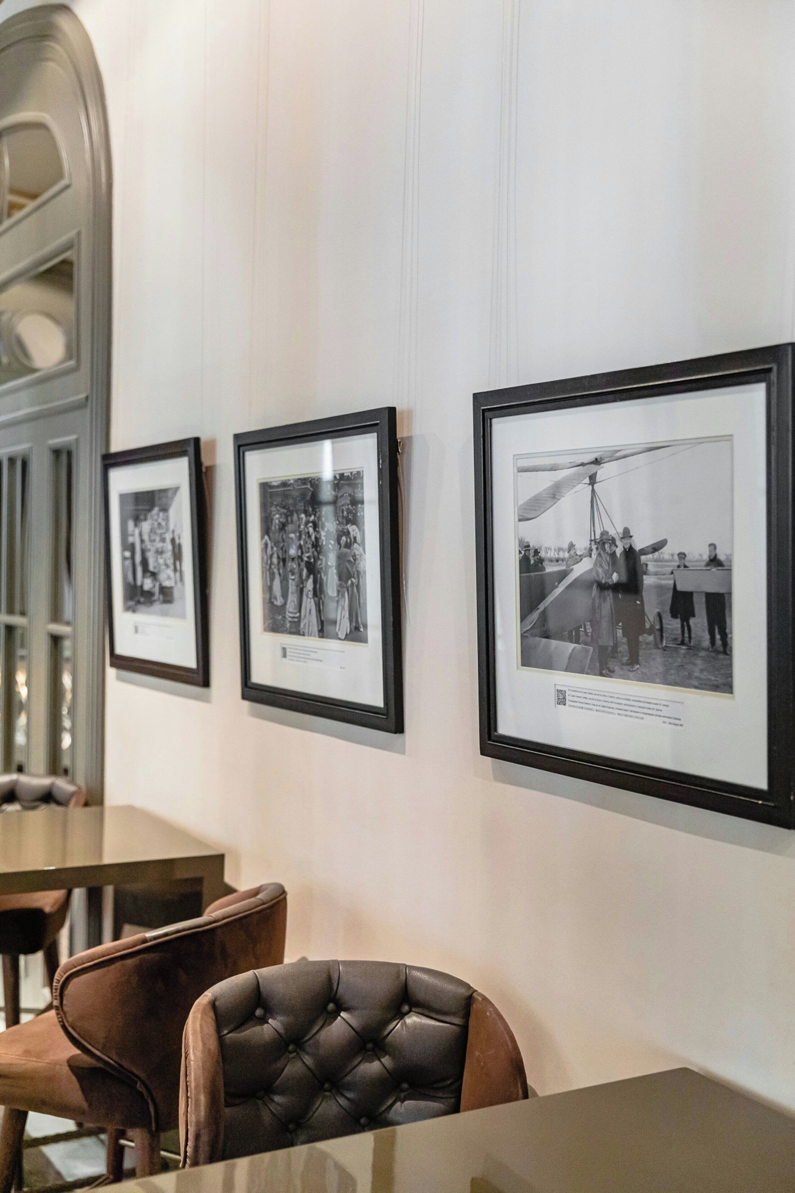 A dining area with framed black and white photographs on the wall, a leather chair, and a glass table.
