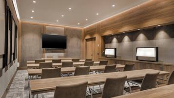 A conference room with multiple tables and chairs, a large flat-screen TV, and two smaller monitors on the wall.