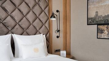 Una habitación de hotel con un cabecero capitonado, una mesita de noche con una lámpara y un cuadro enmarcado en la pared.